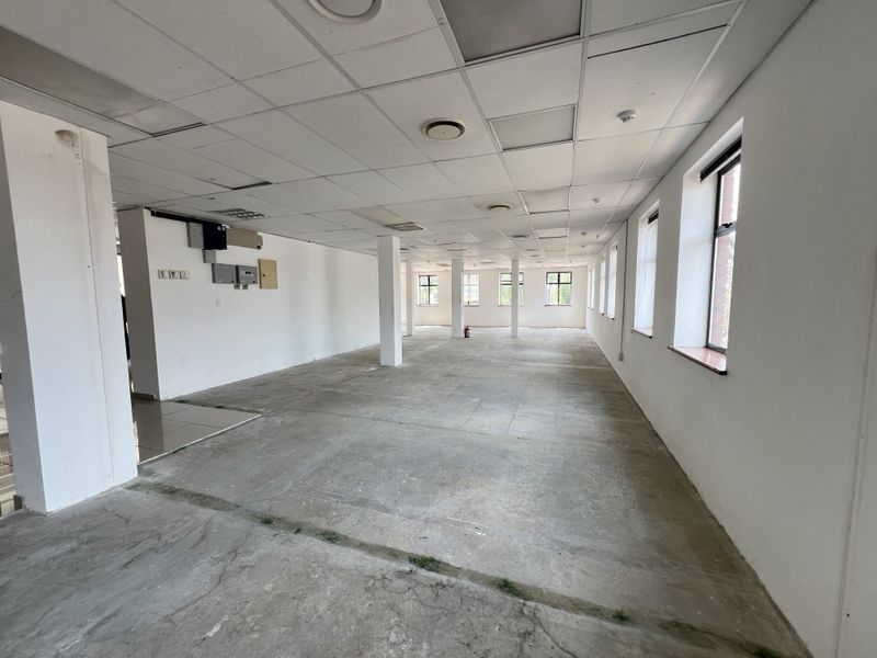 A spacious, open-plan office area featuring a suspended ceiling, structural columns, and large windows, currently in a shell condition ready for fit-out.