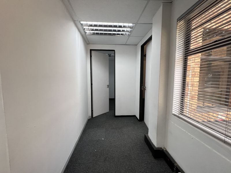 A functional office hallway featuring carpeted flooring, recessed ceiling lighting, and venetian blinds, providing access to multiple office rooms.