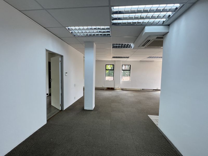 A spacious, open-plan office area featuring carpeted flooring, a suspended ceiling with recessed lighting, and integrated air conditioning.
