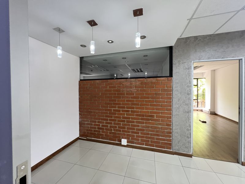 Modern office space featuring an exposed brick feature wall, glass partition, tiled flooring, and contemporary pendant lighting, offering a clean and professional work environment.