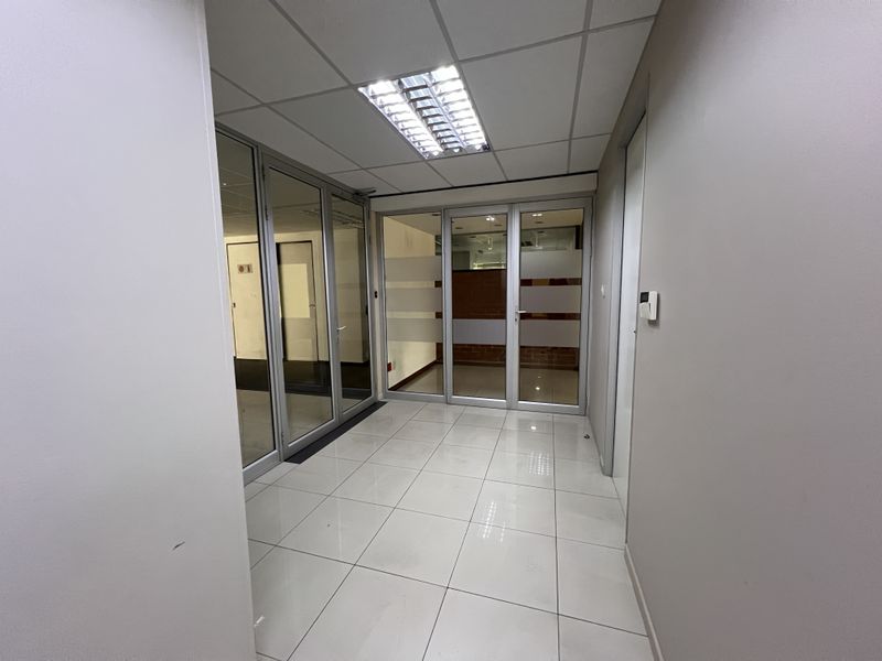 A clean, modern office space featuring tiled flooring, suspended ceilings with recessed lighting, and glass partition walls for a professional, open-plan feel.