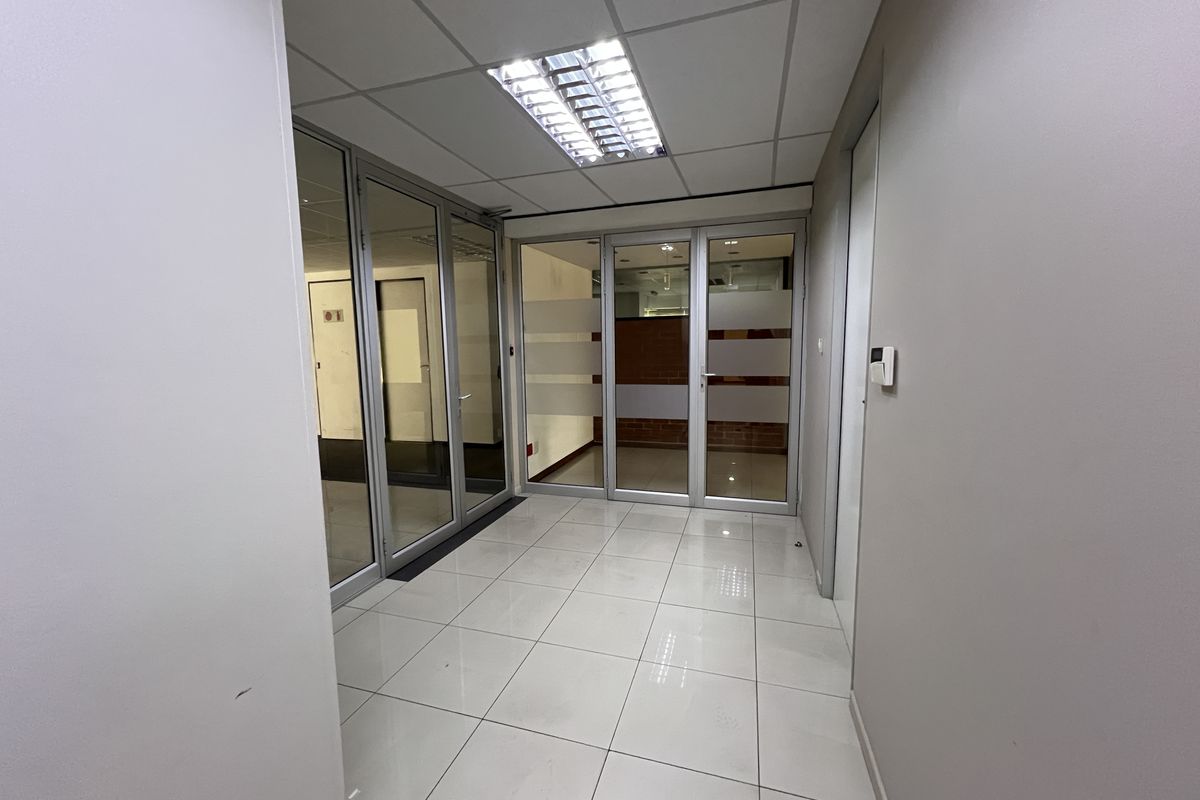 A clean, modern office space featuring tiled flooring, suspended ceilings with recessed lighting, and glass partition walls for a professional, open-plan feel.
