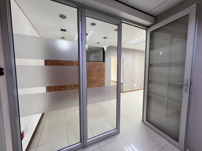 Modern office space featuring glass partitions, exposed brick accents, tiled flooring, and recessed lighting, offering a clean and professional environment.