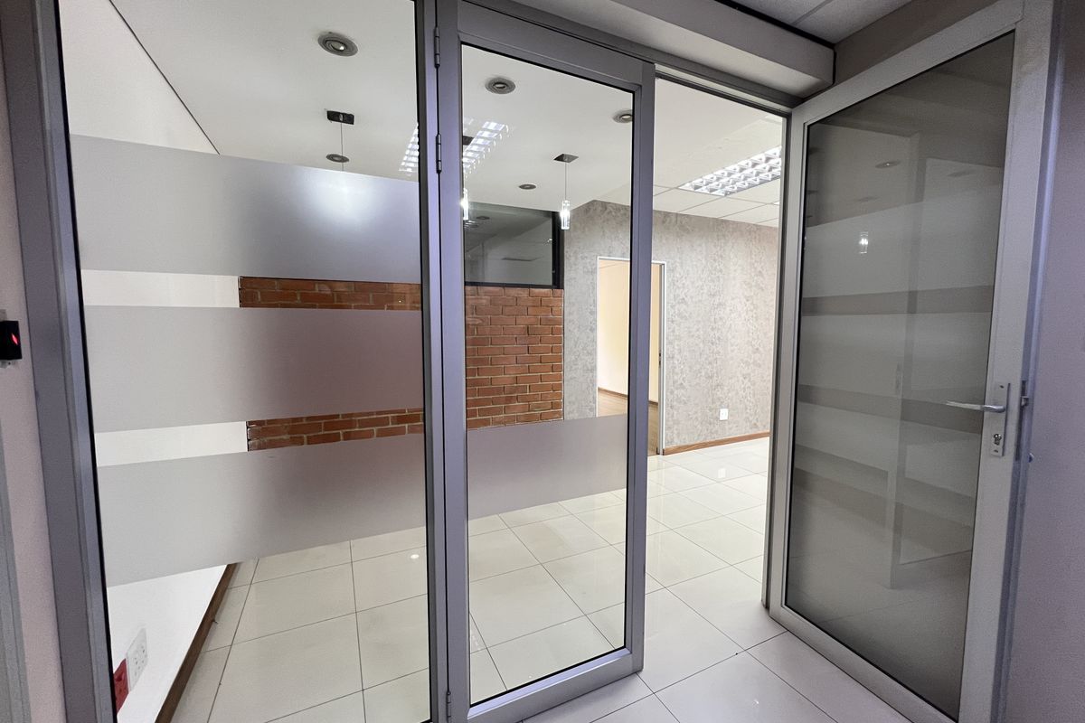 Modern office space featuring glass partitions, exposed brick accents, tiled flooring, and recessed lighting, offering a clean and professional environment.