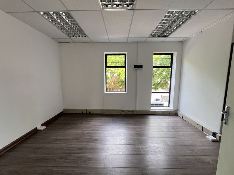 A clean, empty office space featuring laminate flooring, suspended ceilings with recessed lighting, and integrated skirting trunking for electrical connectivity.