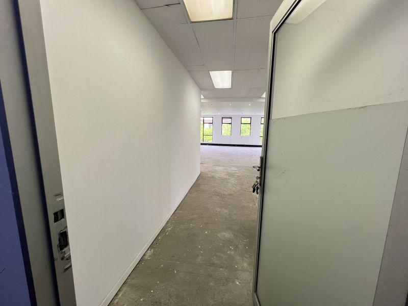 An empty, open-plan office space featuring a suspended ceiling, recessed lighting, and large windows, currently awaiting flooring installation and final finishes.