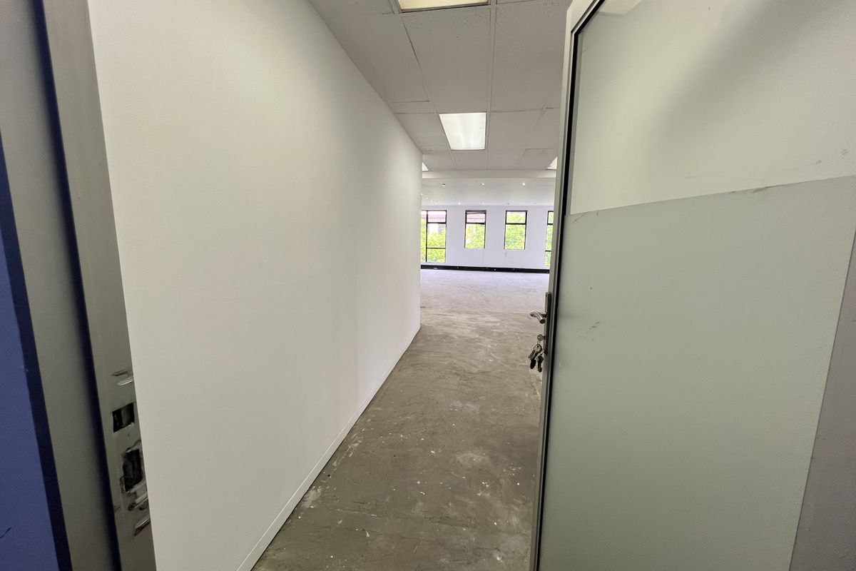 An empty, open-plan office space featuring a suspended ceiling, recessed lighting, and large windows, currently awaiting flooring installation and final finishes.