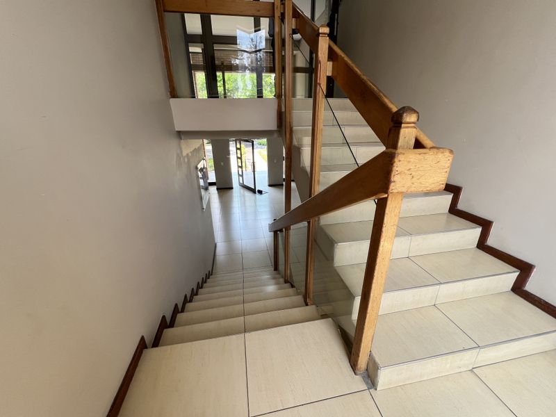 A bright entrance foyer featuring a tiled staircase with a wooden handrail and glass balustrade, leading to a glass-paneled front door.