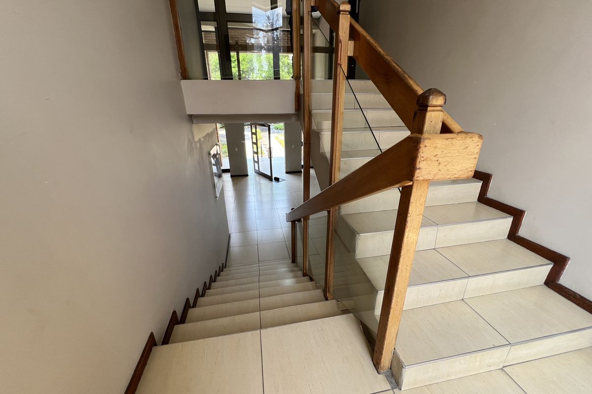 A bright entrance foyer featuring a tiled staircase with a wooden handrail and glass balustrade, leading to a glass-paneled front door.