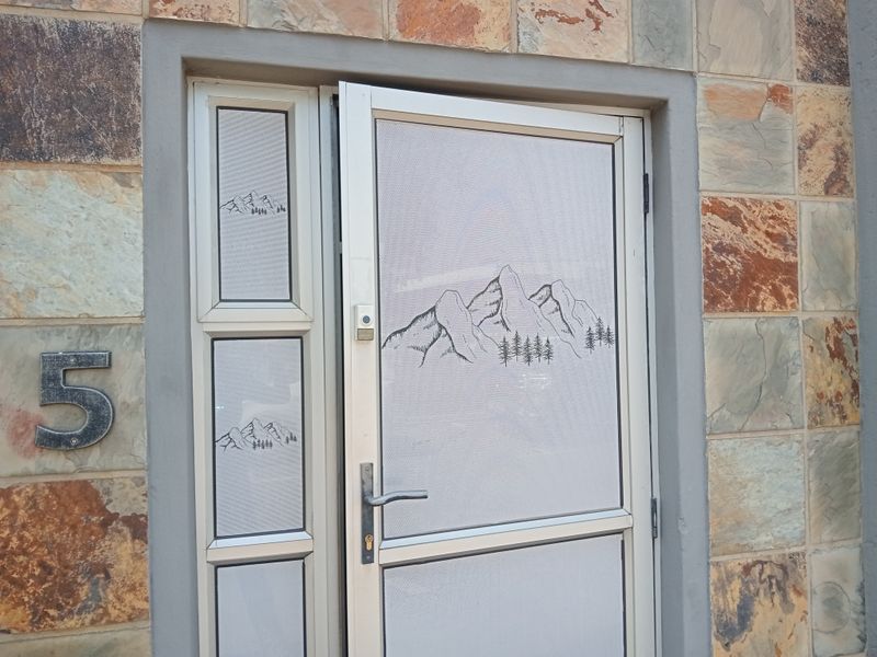 Main entrance featuring a security screen door with mountain graphic detail, set against a natural stone-clad exterior wall.
