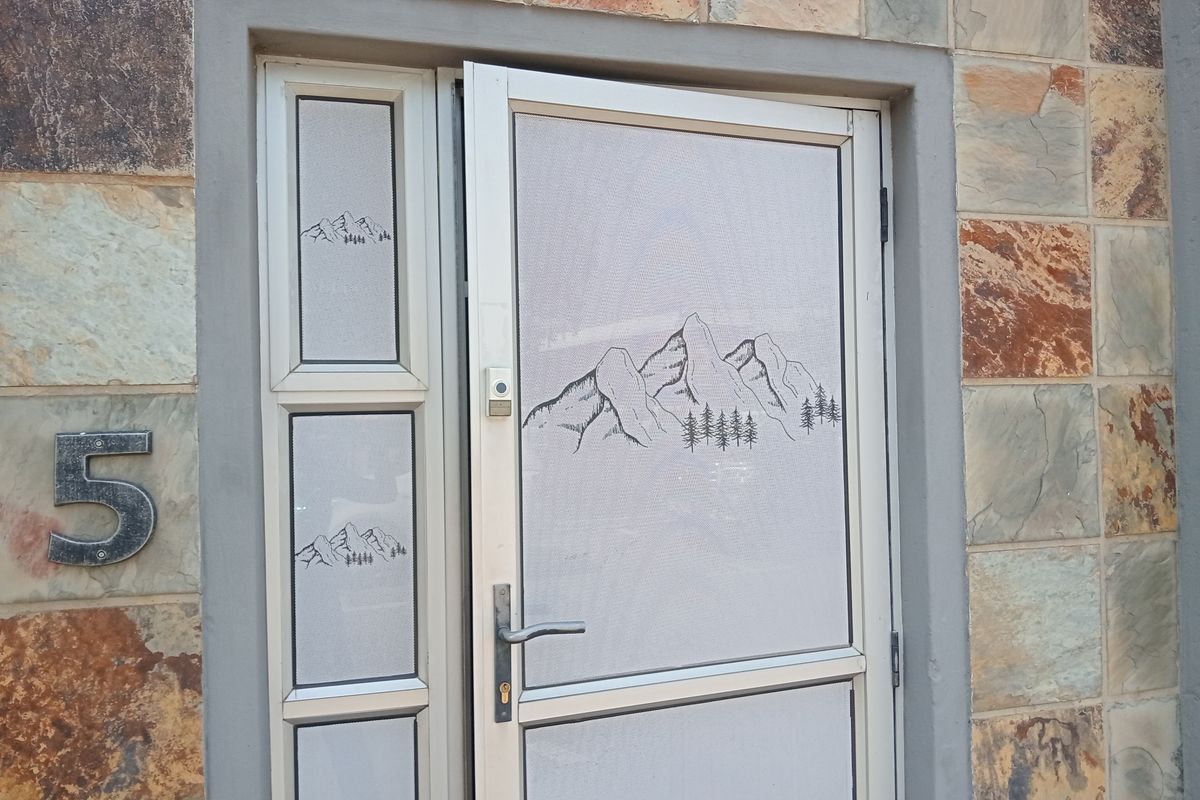 Main entrance featuring a security screen door with mountain graphic detail, set against a natural stone-clad exterior wall.