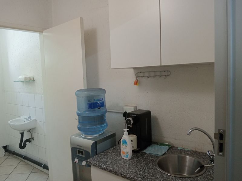 A functional scullery or kitchenette area featuring a stainless steel sink, granite countertop, wall-mounted cabinetry, and an adjacent small washroom area.