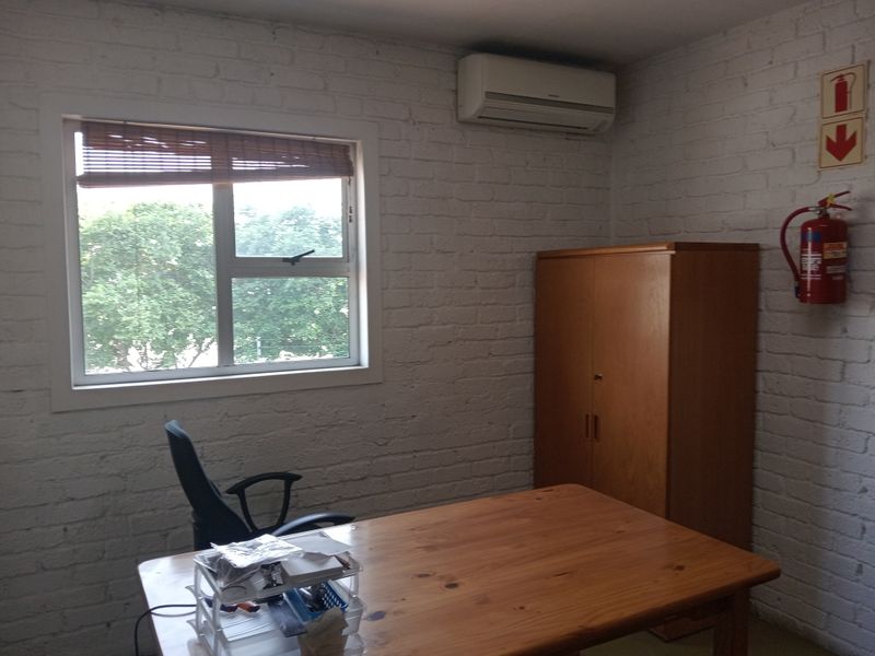 A functional office space featuring painted brick walls, an installed air conditioning unit, and essential fire safety equipment.