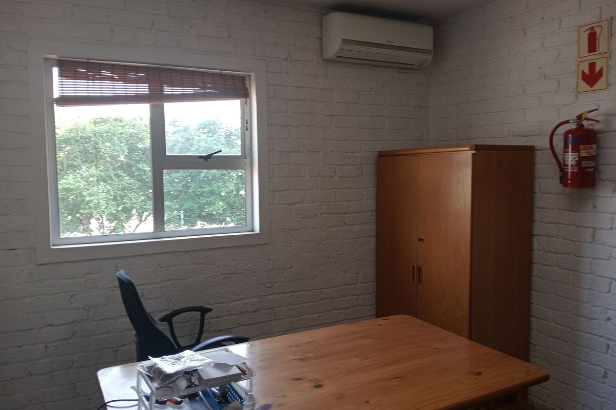 A functional office space featuring painted brick walls, an installed air conditioning unit, and essential fire safety equipment.