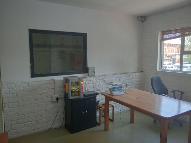 A functional office space featuring exposed white-painted brick walls, a large window, and integrated security camera, suitable for a professional work environment.