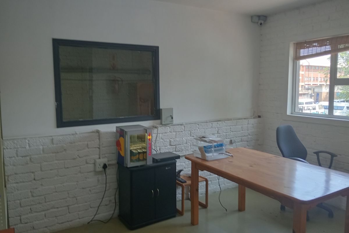 A functional office space featuring exposed white-painted brick walls, a large window, and integrated security camera, suitable for a professional work environment.