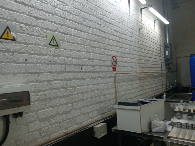 Industrial utility space featuring exposed white-painted brick walls, electrical distribution board, wall-mounted water heater, and stainless steel sink area.