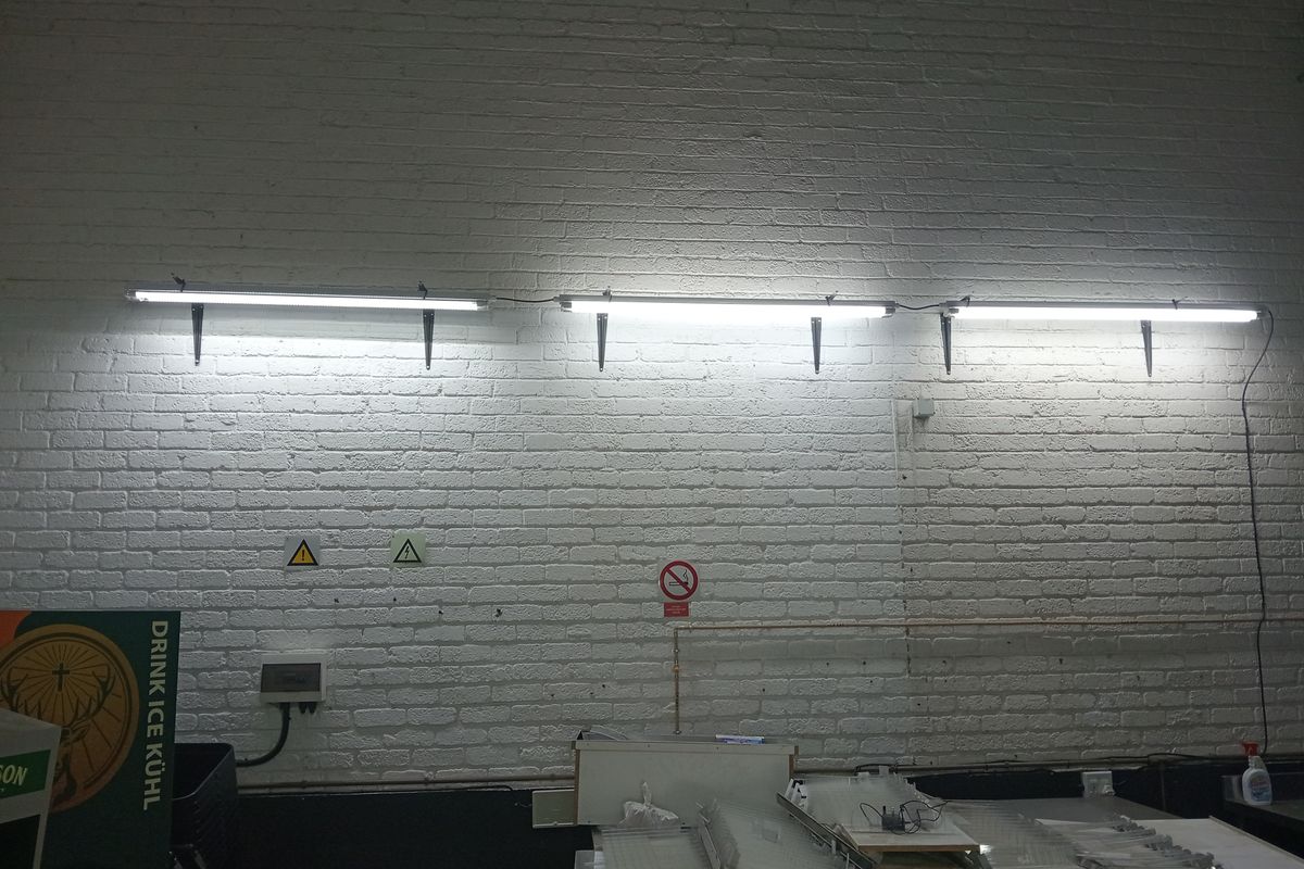 An industrial utility space featuring white painted exposed brick walls and mounted fluorescent strip lighting.