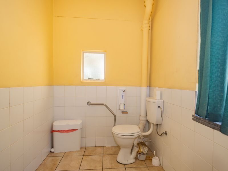 A functional commercial bathroom featuring a toilet, grab rail, tiled finishes, and an obscured glass window.