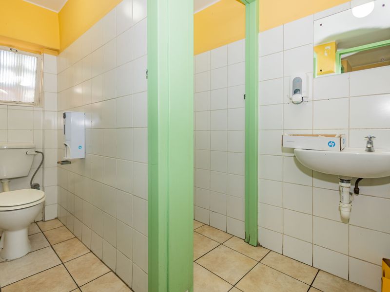 A functional commercial bathroom featuring tiled walls and floors, a wall-mounted basin, and a standard toilet, requiring cosmetic updates to improve its appearance.