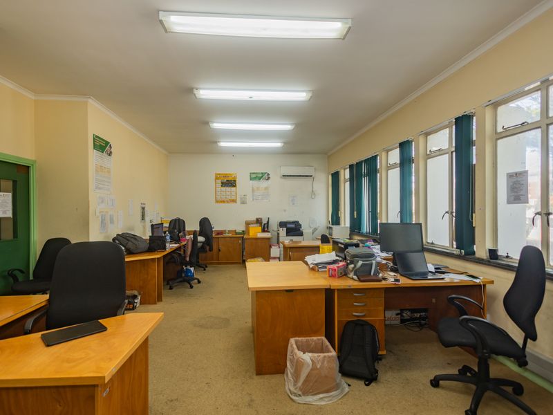 A functional commercial office space featuring large windows for natural light, overhead fluorescent lighting, and a wall-mounted air conditioning unit.