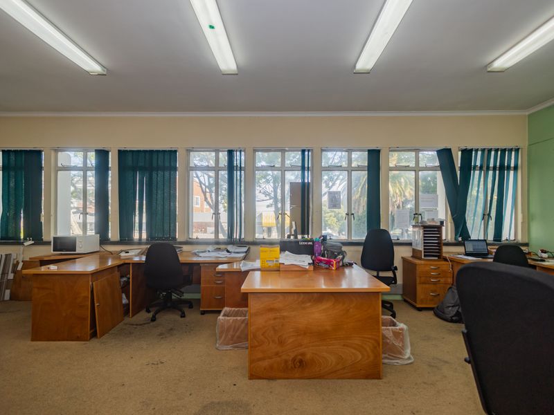 A functional commercial office space featuring large windows, fluorescent lighting, and built-in wooden desk units with carpeted flooring.