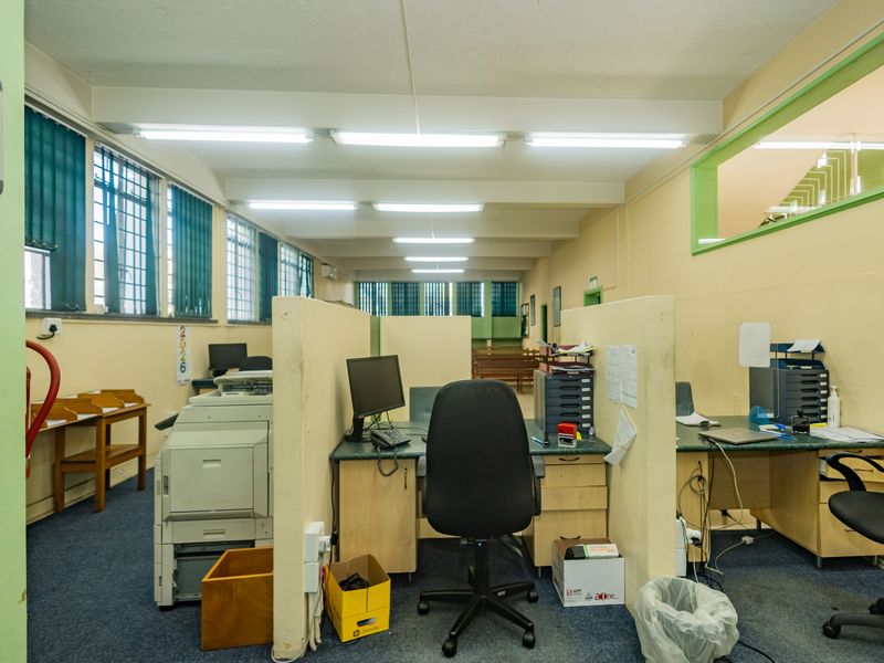 A functional commercial office space featuring built-in partitions, fluorescent lighting, and security bars on the windows.
