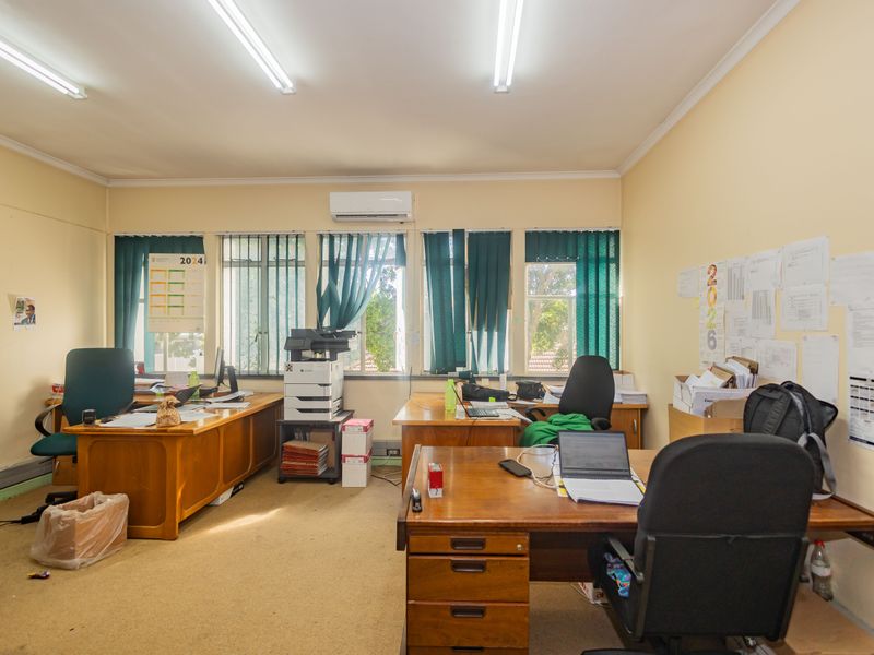A functional commercial office space featuring carpeted flooring, large windows for natural light, and a wall-mounted air conditioning unit.