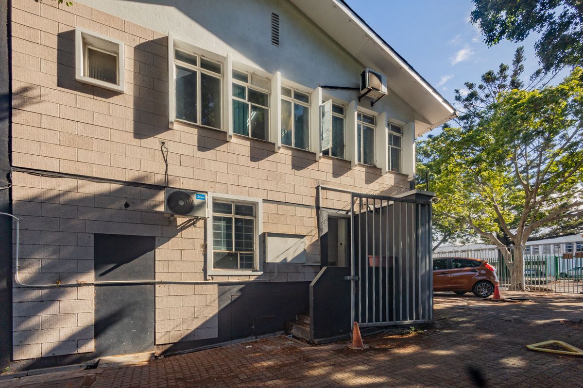 Rear exterior view of a commercial building featuring blockwork walls, multiple casement windows, and a secure gated entrance area with paved access.