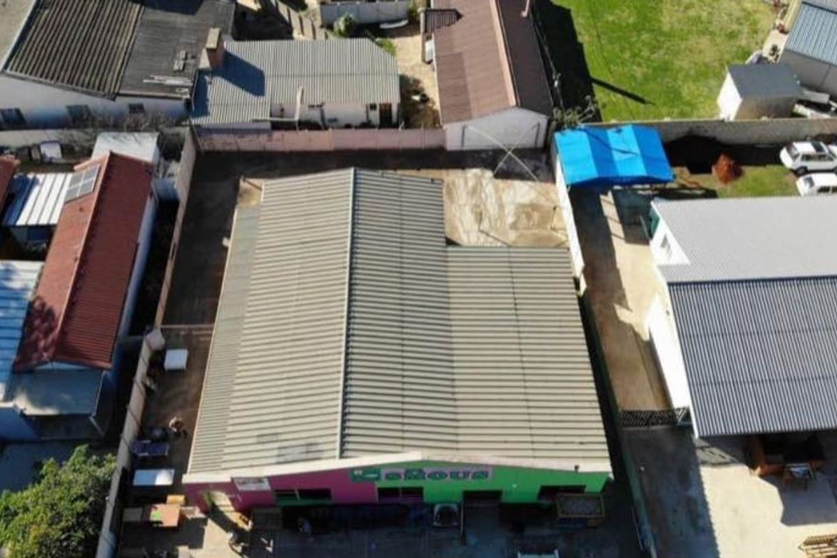 Aerial view of a commercial property featuring a metal-roofed building with a paved yard area and perimeter walling.