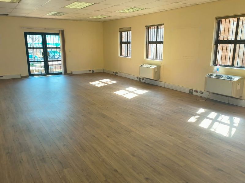 Spacious, empty office area featuring laminate flooring, suspended ceilings, wall-mounted air conditioning units, and security bars on windows.