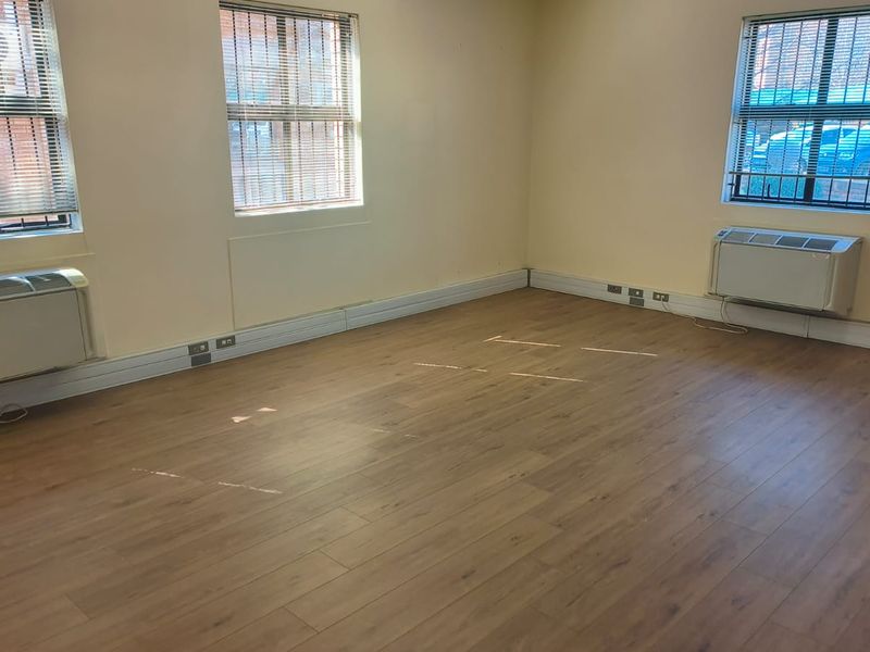 A bright, empty office space featuring laminate flooring, multiple windows with blinds, and wall-mounted air conditioning units.