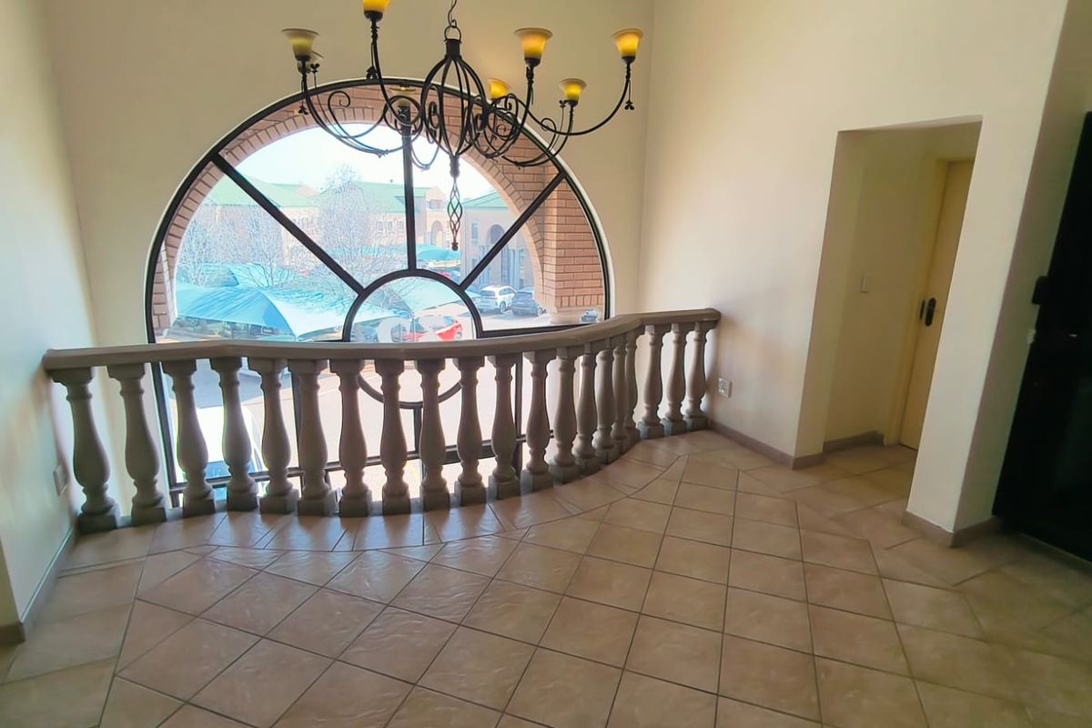 A spacious landing area featuring a large arched window, decorative stone balustrade, and elegant wrought iron chandelier, providing ample natural light.