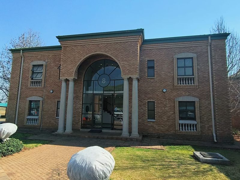 Front elevation of a two-story brick office building featuring an arched entrance with columns and a paved walkway.