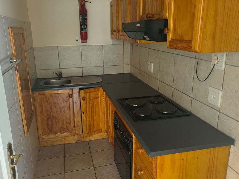 Compact office kitchenette featuring wooden cabinetry, a built-in oven with electric hob, extractor fan, and tiled backsplash.