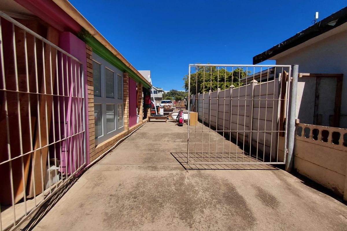 A narrow exterior driveway or side access area featuring concrete paving, metal security gates, and painted brick wall finishes.