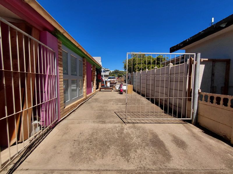 A narrow exterior driveway or side access area featuring concrete paving, metal security gates, and painted brick wall finishes.