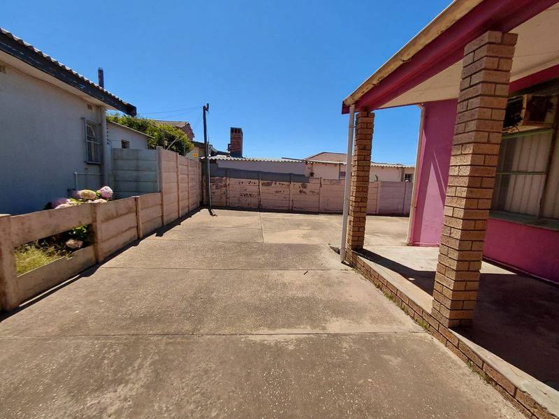 A rear exterior view of the commercial property featuring a concrete paved courtyard, covered patio area with brick pillars, and perimeter boundary walls.