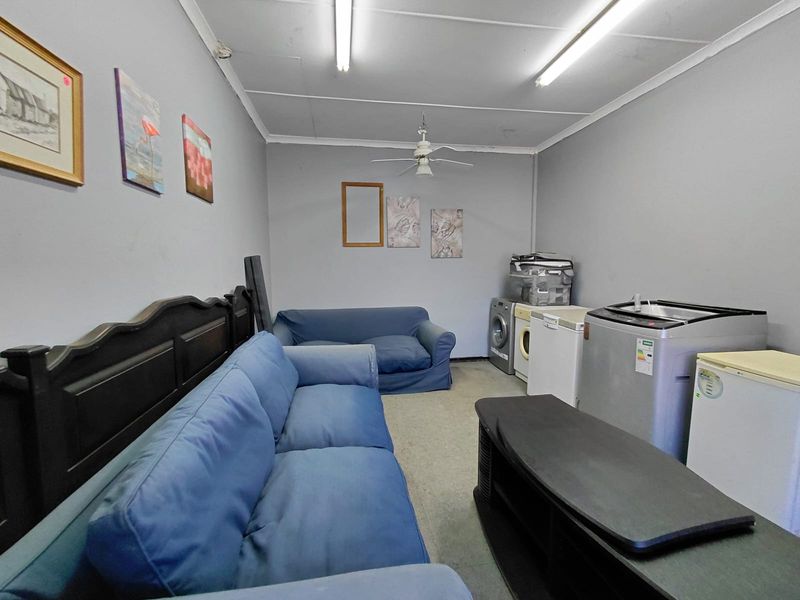 A multi-purpose utility space featuring fluorescent lighting, ceiling fan, and plumbing connections suitable for laundry appliances.