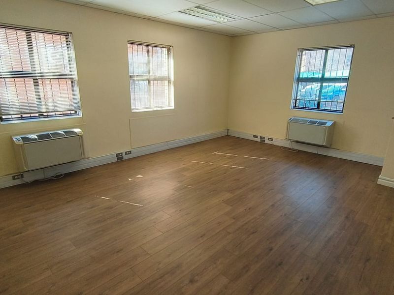 A bright, empty office space featuring laminate flooring, suspended ceilings, recessed lighting, and wall-mounted air conditioning units.