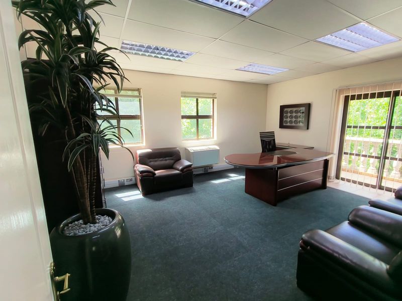 A professional office space featuring a suspended ceiling, recessed lighting, wall-mounted air conditioning, and access to an outdoor balcony through sliding glass doors.