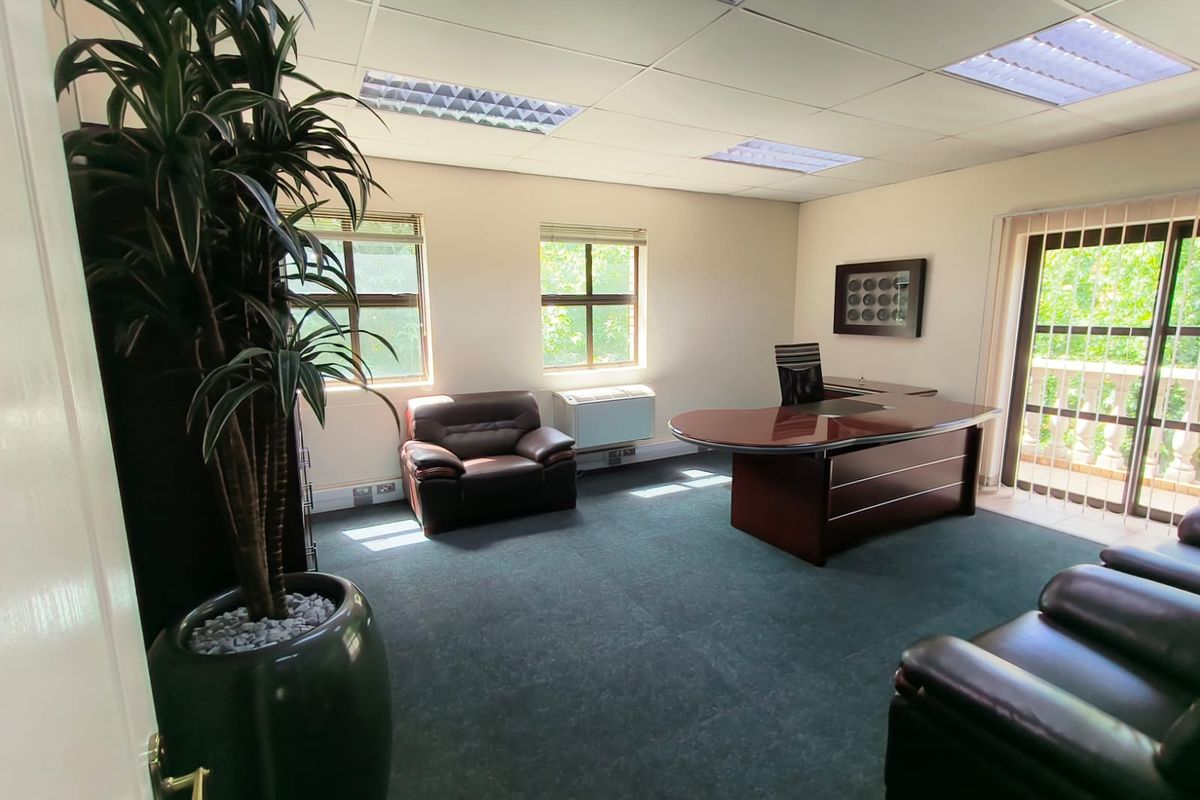 A professional office space featuring a suspended ceiling, recessed lighting, wall-mounted air conditioning, and access to an outdoor balcony through sliding glass doors.