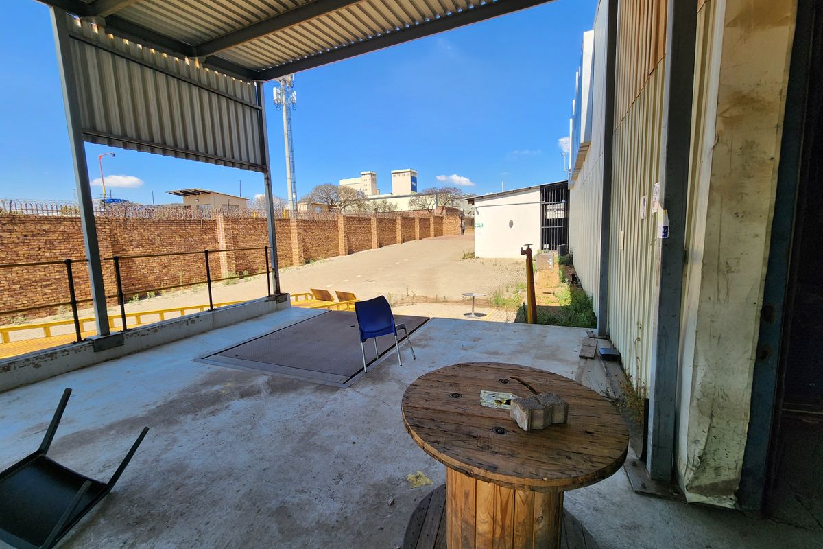 A covered industrial loading bay area featuring a concrete floor, metal roof structure, and access to a secure, walled outdoor yard space.