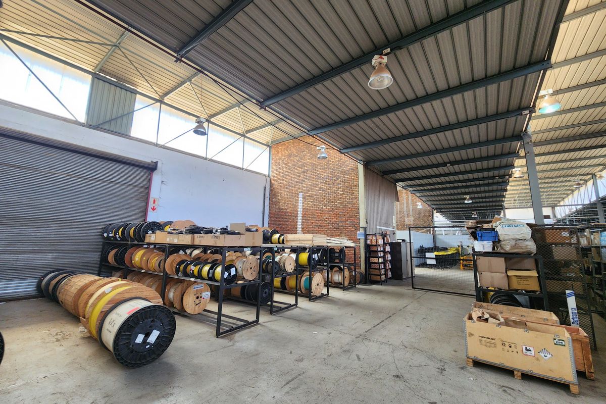 Spacious industrial warehouse area featuring high ceilings with exposed steel trusses, concrete flooring, and large roller shutter access, suitable for storage or manufacturing operations.