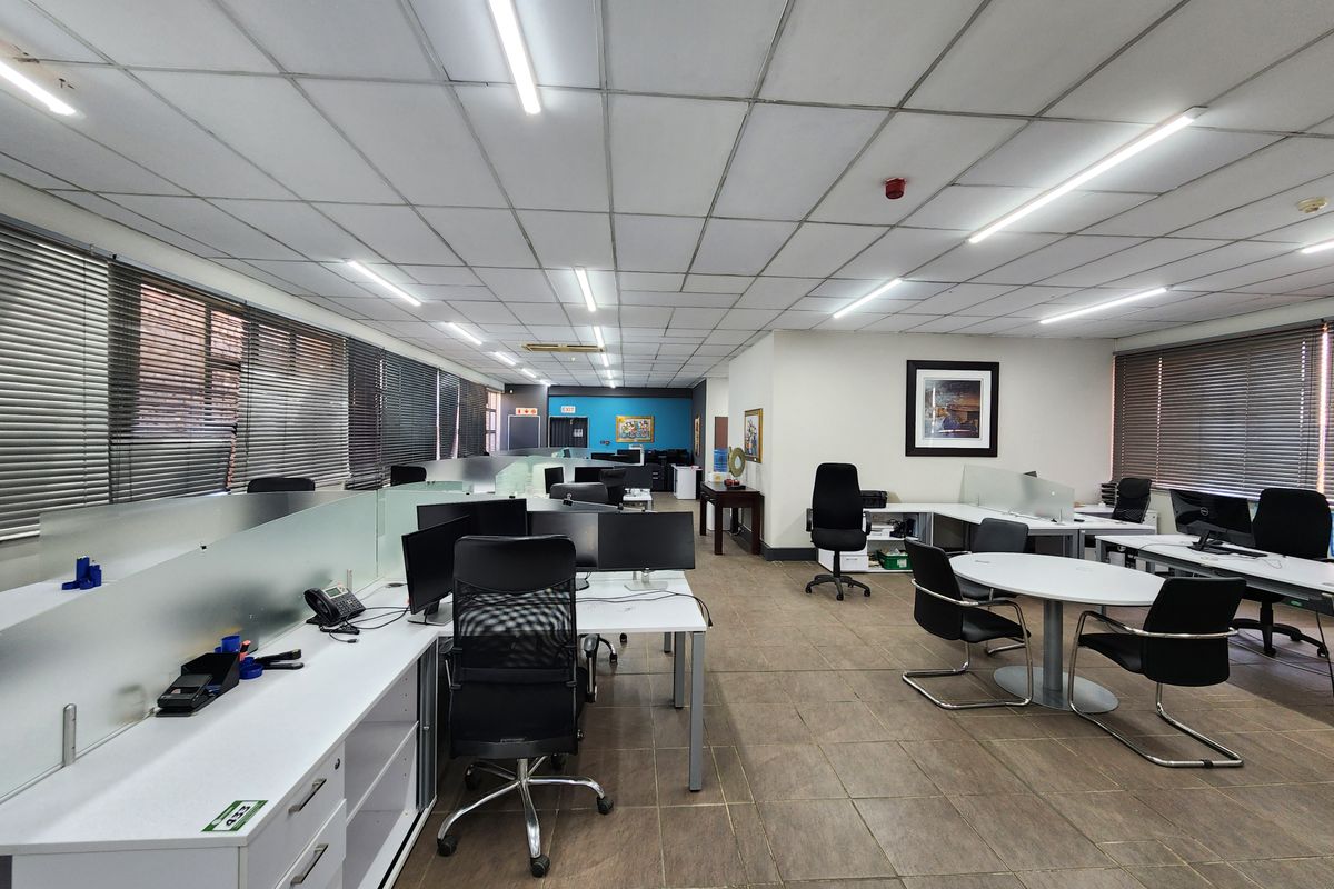 Spacious open-plan office area featuring suspended ceilings, tiled flooring, and large windows with venetian blinds, providing a functional professional workspace.