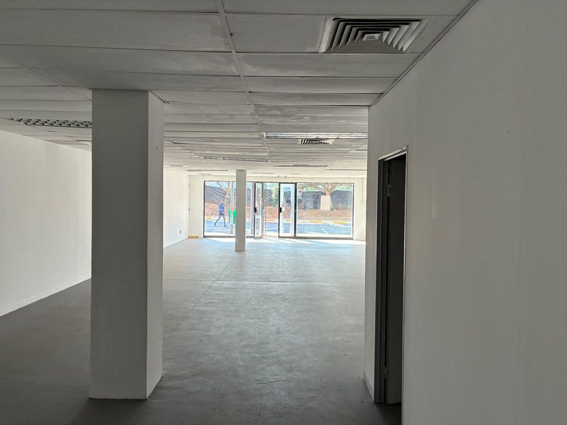 An open-plan retail space featuring a suspended ceiling with integrated air conditioning, concrete flooring, and large glass windows providing natural light.