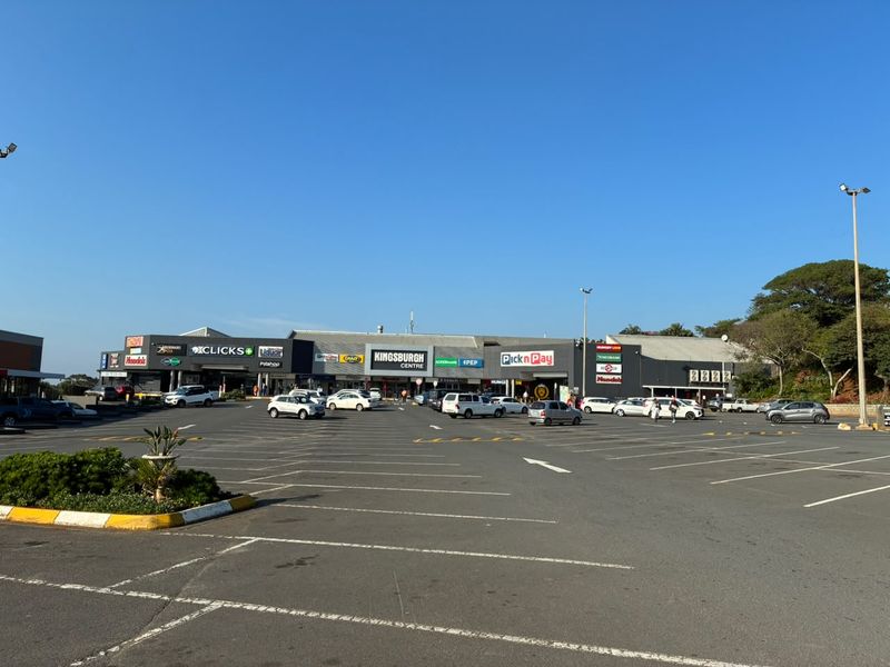 A wide-angle view of the Kingsburgh Centre retail complex, featuring a large asphalt parking area and multiple commercial storefronts with prominent signage.