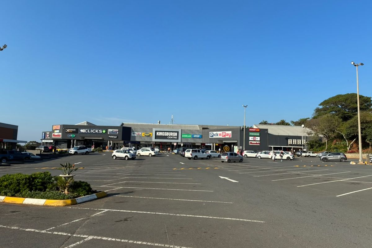 A wide-angle view of the Kingsburgh Centre retail complex, featuring a large asphalt parking area and multiple commercial storefronts with prominent signage.