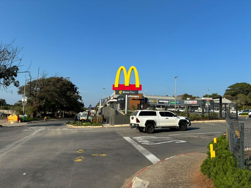 Exterior view of a retail shopping centre featuring a McDonald's drive-thru and prominent commercial signage with paved access roads.