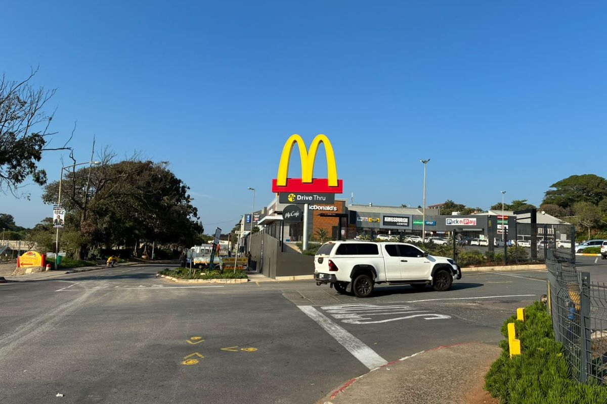 Exterior view of a retail shopping centre featuring a McDonald's drive-thru and prominent commercial signage with paved access roads.